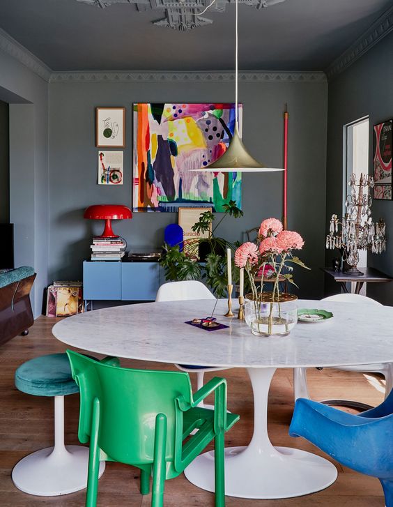 a catchy home office with grey walls and a ceiling, a white table, colorful mismatching chairs, a blue credenza and colorful artwork