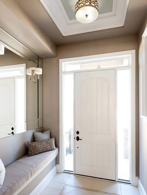 a chic greige entryway with an oversized mirror, lamps and a built-in greige upholstered bench is a lovely space to be
