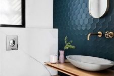 a chic modern powder room clad with white marble tiles and navy hex tiles, a floating vanity and a bowl sink, a wall-mounted toilet
