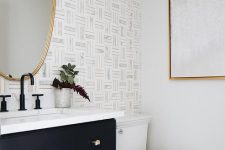 a chic modern powder room with a wallpaper accent wall, a black vanity, an asymmetrical mirror and gold touches