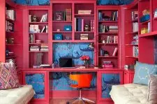 a colorful home office with navy printed wallpaper, a deep red stotage unit with a built-in desk, an orange chair and a bold printed rug