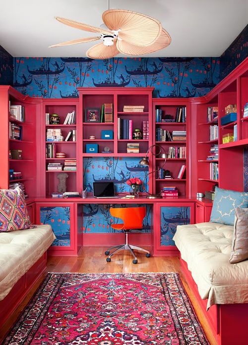 a colorful home office with navy printed wallpaper, a deep red stotage unit with a built-in desk, an orange chair and a bold printed rug