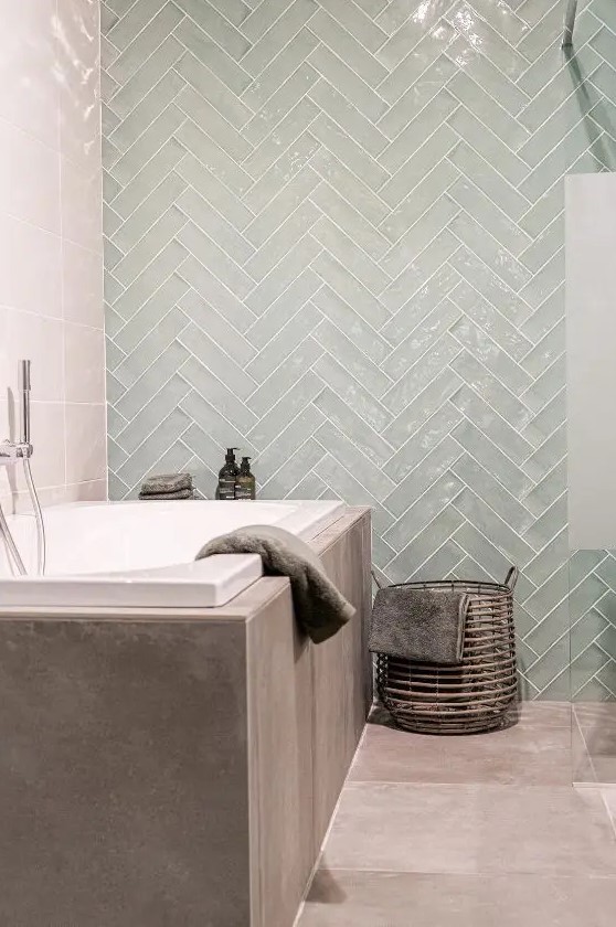 a contemporary bathroom with a greige tile floor, a bathtub clad wtih greige concrete, an aqua chevron tile accent wall