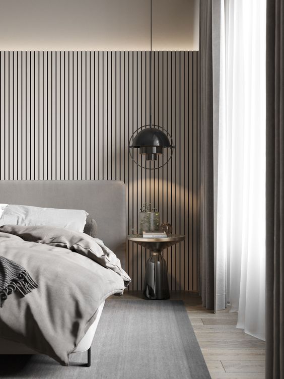 a contemporary geige bedroom with a wood slat headboard wiht lights, a grey upholstered bed with grey bedding, a black pendant lamp