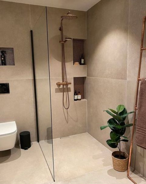 a contemporary greige bathroom clad with large scale stone tiles, with niche shelves, white appliances and black touches