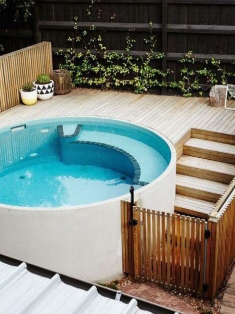 a contemporary round pool with a light-colored wooden deck and some potted plants to make the space fresh