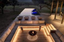 a contemporary sunken patio with a wooden deck, built-in benches with neutral upholstery, a fire pit and some stools