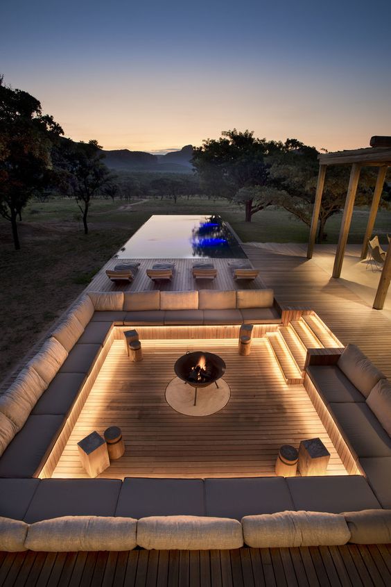 a contemporary sunken patio with a wooden deck, built-in benches with neutral upholstery, a fire pit and some stools