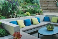 a contemporary sunken patio with built-in benches, colorful pillows and a coffee table plus greenery and blooms around