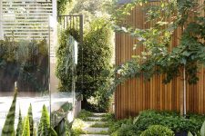 a contemporary townhouse garden with stone tiles, greenery, trees and a living wall plus some lights