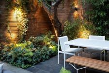 a contemporary townhouse garden with stone tiles, minimalist furniture of wood and metal, lush textural greenery and a tree growing