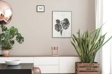 a cool modern greige living room with a white storage unit, a black coffee table, potted plants, some artwork and a leather blanket on the floor