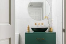 a cool modern powder room with white large scale tiles, a printed tile floor, a green vanity with a black bowl sink, gilded touches for more chic