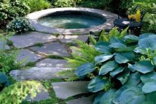 a cute hot tub space right in the garden, with a stone path, a built-in tub clad with stone, a couple of chairs for placing drinks