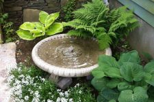 a cute outdoor nook with a classic bowl fountain, some greenery and blooms and a stone pathway next to it