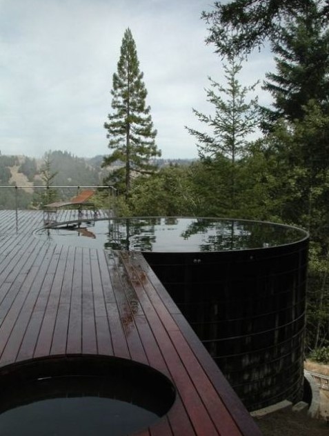 a dark stained wooden deck with a large and deep round pool that features amazing views of the nature around
