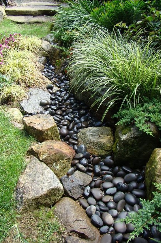 a dry creek bed with dark pebbles and lined up with large rocks and grasses is a cool idea