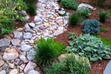 a dry stream idea with large pebbles and rocks plus green grasses around and some blooms