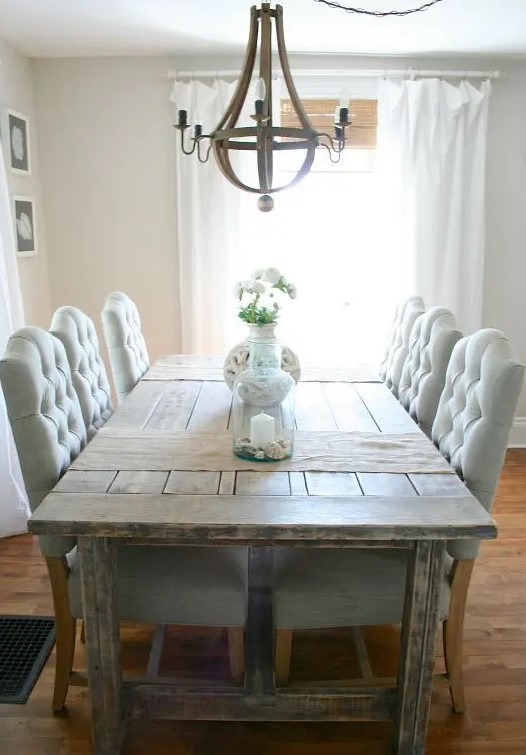 a farmhouse dining room with a shabby chic wooden table, blue upholstered chairs, a rustic chandelier and wicker shades