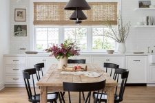 a farmhouse dining space with a stained table and black chairs, black pendant lamps, blooms and greenery