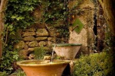 a flow of water fountain made of a faucet and some bowls and surrounded with greenery is a lovely solution