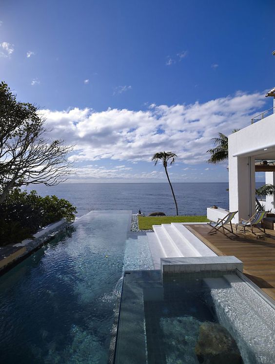 a gorgeous infinity pool with a sea view, a wooden deck and steps plus greenery and trees around is a fantastic place