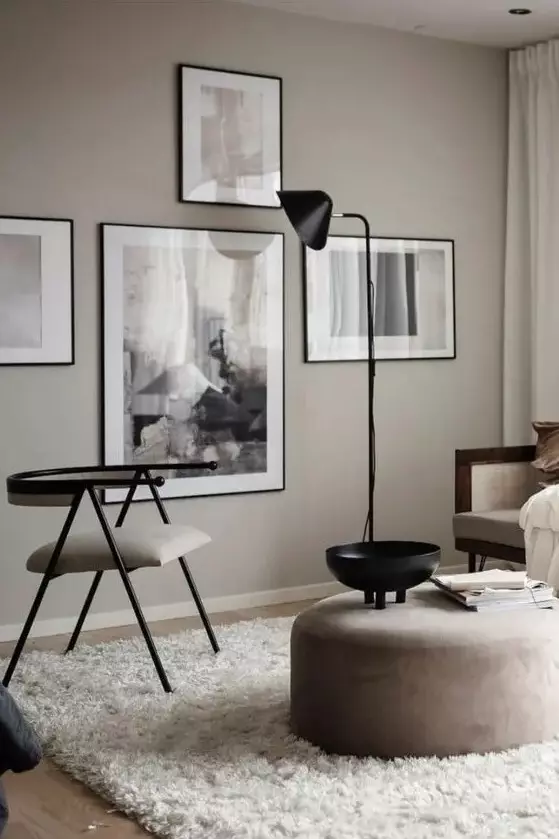 a greige Scandi-inspired living room with a cool gallery wall, neutral seating furniture, a round pouf, a cool rug and a black floor lamp
