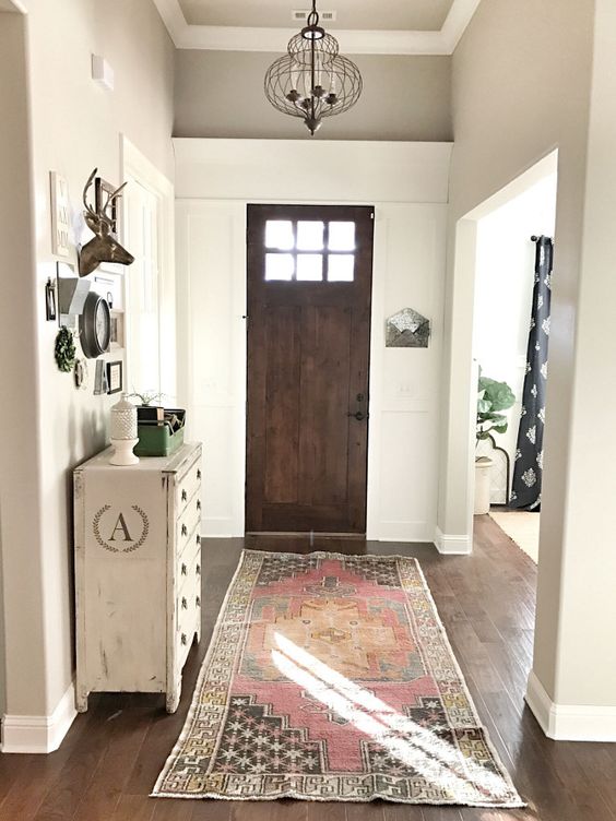 a greige boho entryway with a neutral dresser, a bold printed rug, a dark-stained door, a catchy rustic gallery wall
