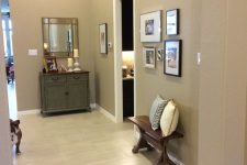 a greige entryway with a vintage cabinet, a wall mirror, a gallery wall and a dark-stained bench with pillows