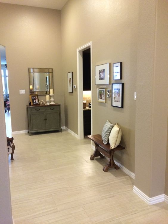 a greige entryway with a vintage cabinet, a wall mirror, a gallery wall and a dark stained bench with pillows