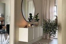 a greige entryway with a white console table, a round mirror, a potted tree and some matching greige curtains is a chic space