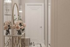 a greige entryway with an elegant console tabl, blush blooms, a round mirror and a white marble floor