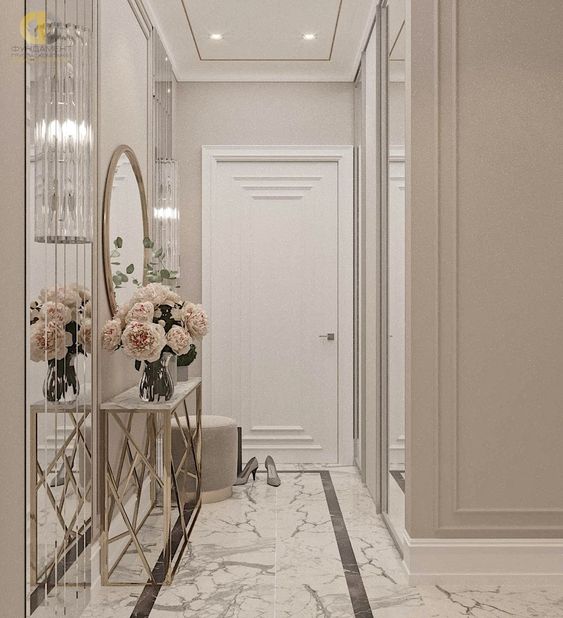 a greige entryway with an elegant console tabl, blush blooms, a round mirror and a white marble floor