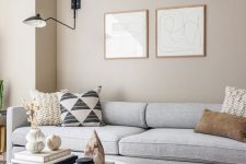 a greige living room with a grey sofa and printed pillows, a round white coffee table and a cool black sconce for an accent