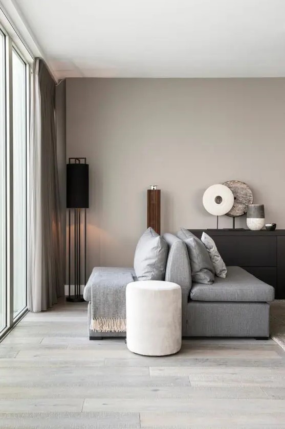a greige living room with grey furniture, a black credenza, some floor and table lamps, greige curtains is a cozy and soothing space