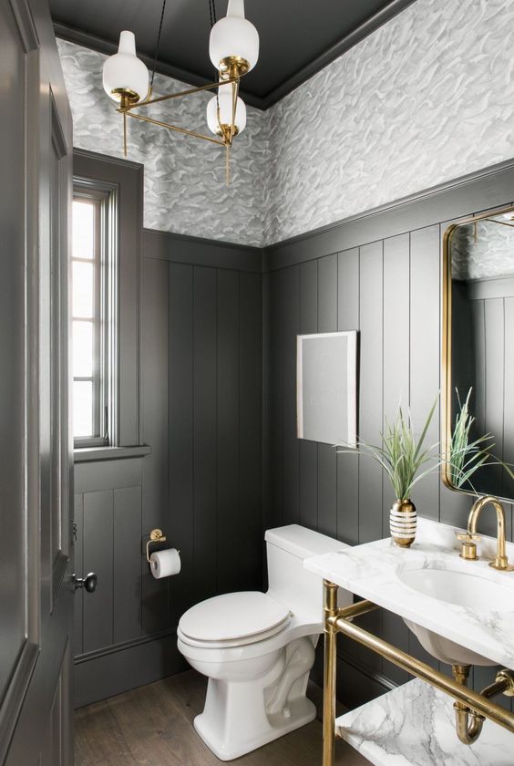 a grey modern farmhouse powder room with wallpaper and paneling, a stone vanity with a sink, a chic chandelier and a plant
