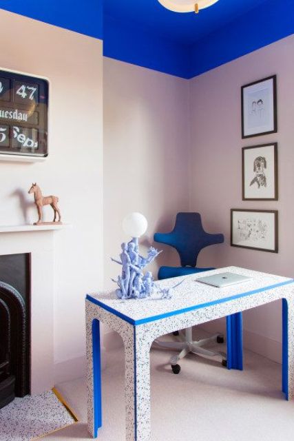 a jaw-dropping blush and electric blue home office with a vintage fireplace, a catchy terrazzo desk, a blue chair and a blue ceiling