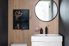 a laconic contemporary powder room with a wood accent wlal, a floating vanity and white appliances, an artwork and a round mirror