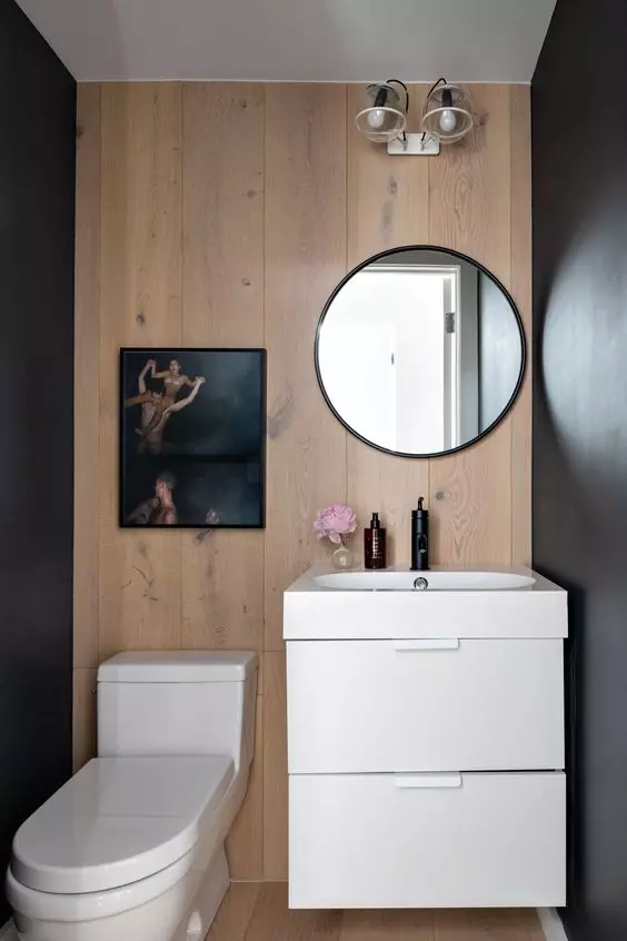 a laconic contemporary powder room with a wood accent wlal, a floating vanity and white appliances, an artwork and a round mirror