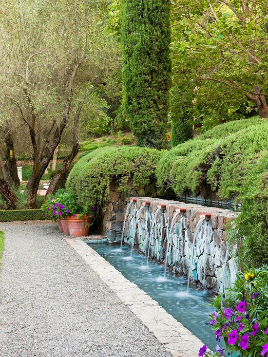 a large and chic fountain of stone and with multiple faucets, with blooms and greenery around