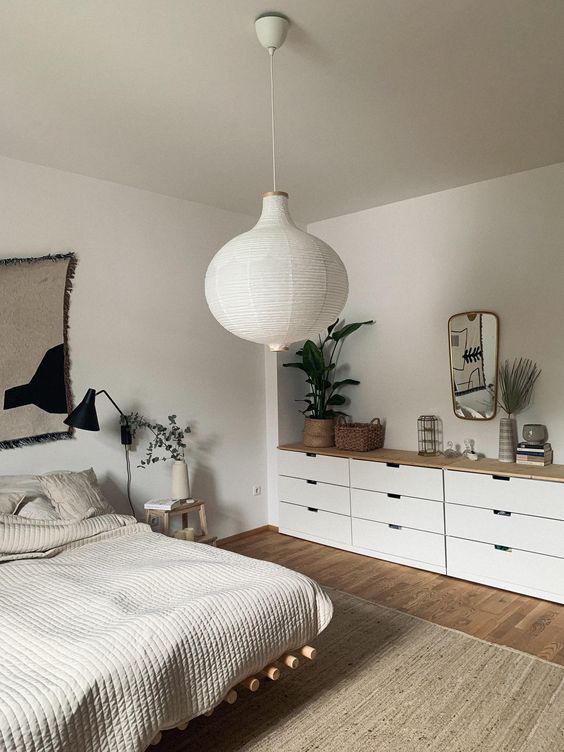a light grey Scandi bedroom with a greige ceiling, a floating bed with neutral bedding, a large dresser and a paper pendant lamp