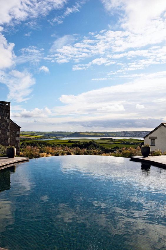 a lovely infinity pool with a view of the plants, green fields and a lake, with stone houses around the pool is amazing