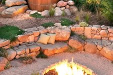 a lovely outdoor space with a fire pit space with a built-in stone bench and wood slice stools, a hot tub surrounded with rocks