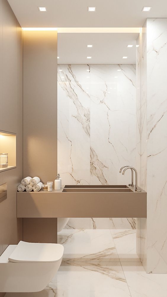 a luxurious minimalist powder room with white marble tiles, a stone built-in sink and built-in lights here and there