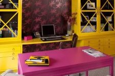 a maximalist home office with bold wallpaper, a hot pink desk and bold yellow storage units, colorful chairs and a pendant lamp