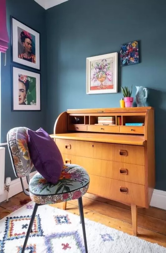 a maximalist working nook with grey walls, a vintage bureau desk, a colorful chair and bold textiles plus a bright gallery wall