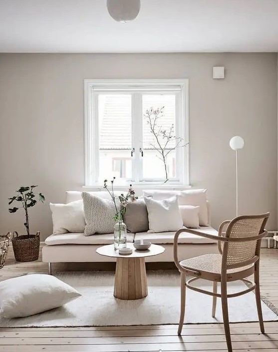 a minimal greige living room with a blush loveseat, a rattan chair, neutral pillows and some greenery