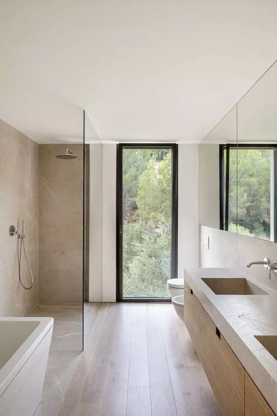 a minimalist bathroom clad with greige stone tiles, a wooden floor, a floating wooden vanity and a floor to ceiling window