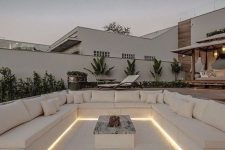 a minimalist creamy sunken patio with upholstered built-in benches, a fire pit in the center and built-in lights