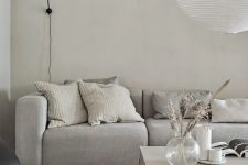 a minimalist greige living room with a grey sofa, a greige stone coffee table, a black sconce and a pendant lamp is amazing